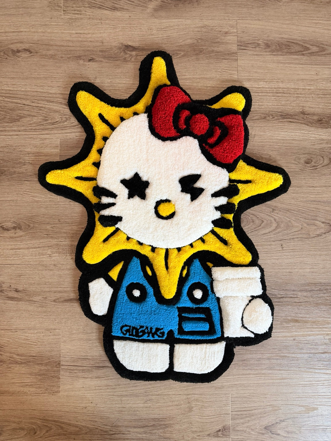 Hand-tufted Hello Kitty-inspired sunburst rug with a red bow, yellow rays, blue outfit and black outline.