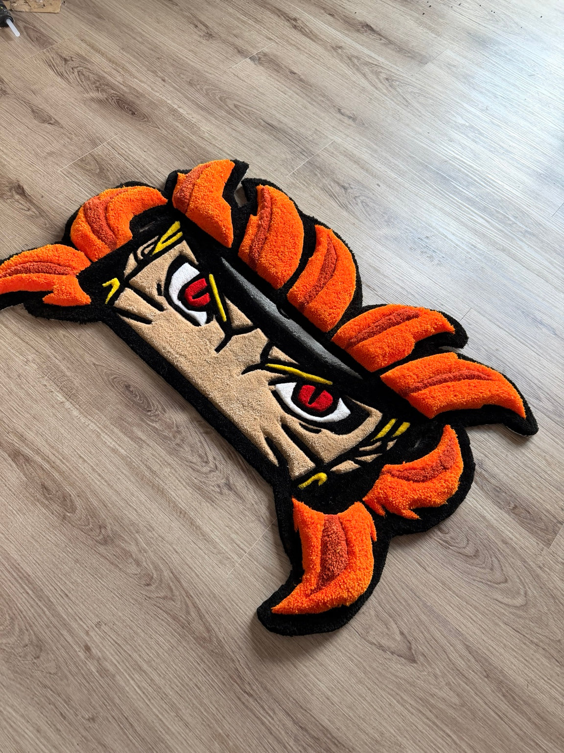 Angled view showing the carved texture and raised orange details of the anime eyes rug.